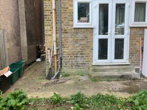 Garden backyard with tools and green bins needing waste clearance in Penge