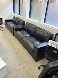 Two black leather sofas with visible wear and tear in an office setting awaiting bulky waste collection"